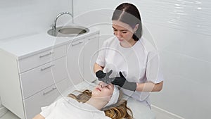 Cosmetologist applies a woman a therapeutic mask on her face. Woman in a spa salon on cosmetic procedures for facial