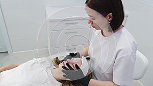 Cosmetologist applies a woman a therapeutic mask on her face. Woman in a spa salon on cosmetic procedures for facial