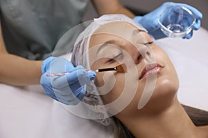 Cosmetologist applying chemical peel product on client`s face in salon