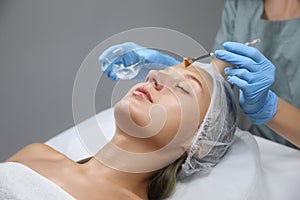 Cosmetologist applying chemical peel product on client`s face in salon