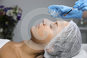 Cosmetologist applying chemical peel product on client`s face in salon