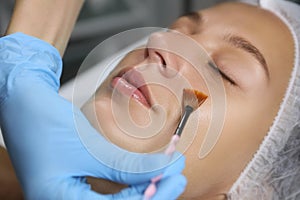 Cosmetologist applying chemical peel product on client`s face in salon, closeup