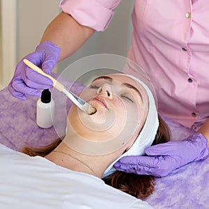 Cosmetologist applying cosmetic mask on the face of a young woman