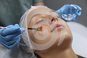 Cosmetologist applying cosmetic product for chemical peeling on client`s face in salon