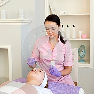 Cosmetologist applying face mask cream on client woman in beauty salon