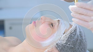 Cosmetologist applying facial moisturizing mask on woman face using brush.