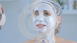Cosmetologist is applying facial moisturizing mask on woman face using brush.
