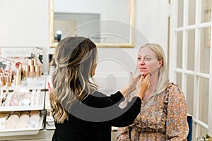 Cosmetologist applying foundation makeup to a blond woman in a makeup chair