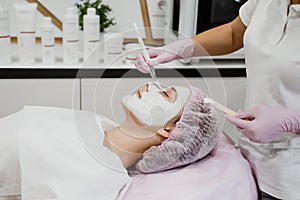 Cosmetologist applying mask on client& x27;s face in spa salon. Young woman getting facial care by beautician at spa salon Acne