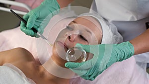 Cosmetologist applying peeling mask on woman face using brush in beauty clinic.