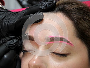 Cosmetologist applying permanent make up eyebrows for a client in a salon