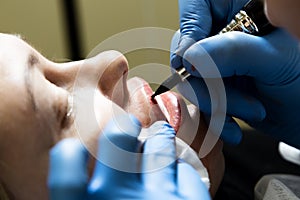 Cosmetologist applying permanent make-up. Young beautiful woman having cosmetic tattoo on her lips. Healthy Spa