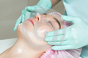 Cosmetologist is applying a white cream on woman`s face