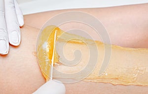 Cosmetologist beautician waxing female legs in the spa center beauty salon