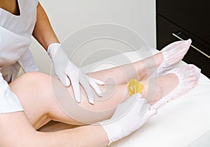 Cosmetologist beautician waxing female legs in the spa center beauty salon photo