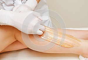 Cosmetologist beautician waxing female legs in the spa center beauty salon photo