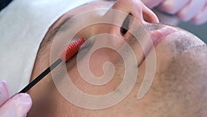 Cosmetologist is bruching eyelashes of man usinf mascara brush, closeup view.