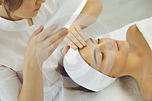 Cosmetologist checking skin elasticity and making examination for young relaxing woman