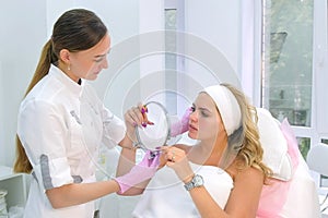 Cosmetologist is consulting woman client who looking at mirror in beauty clinic.