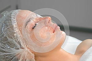 Cosmetologist doctor applies film on cream with anesthesia on woman`s face.
