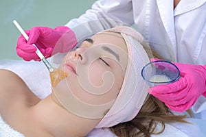Cosmetologist doctor applying mask on woman`s face using brush in beauty clinic.
