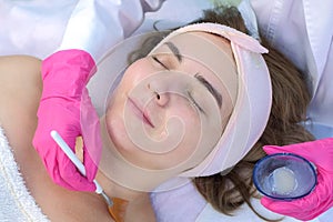 Cosmetologist doctor applying mask on woman`s face using brush in beauty clinic.