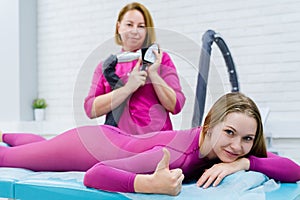 cosmetologist doing anticellulite LPG massage for woman in pink lpg suit. Beauty woman smiling and holds up her finger