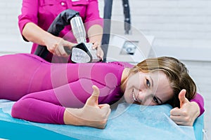 cosmetologist doing anticellulite LPG massage for woman in pink lpg suit. Beauty woman smiling and holds up her finger