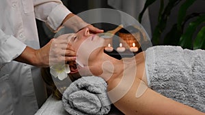 Cosmetologist doing professional face massage with jade stone. Woman receiving face massage in spa