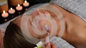 Cosmetologist doing professional face massage using jade roller. Woman receiving face massage in spa
