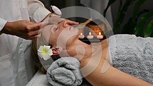 Cosmetologist doing professional face massage using jade roller. Woman receiving neck and face massage