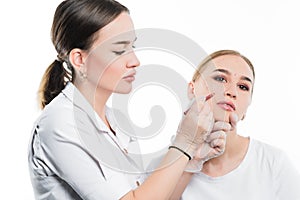 A cosmetologist examines the patient face and plans to perform a series of cosmetic procedures