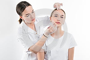 A cosmetologist examines the patient face and plans to perform a series of cosmetic procedures