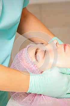 Cosmetologist with gloved hands applies a moisturizing mask with peeling cream on the female face. Facial cosmetology