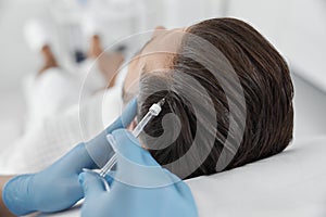 Cosmetologist in gloves does vitamin injection in patient head skin during meso therapy