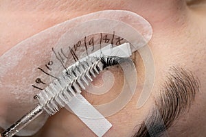 Cosmetologist hand does eyelash extension with eyelash brush