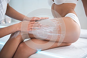 Cosmetologist hands applying white clay on lady hip