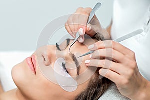 Cosmetologist hands are holding tweezers above the face of young woman