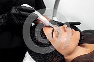 Cosmetologist make face while procedure ultrasound cavitation or facial peeling in cosmetology cabinet.
