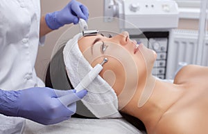 The cosmetologist makes the apparatus a procedure of Microcurrent therapy of a beautiful, young woman in a beauty salon