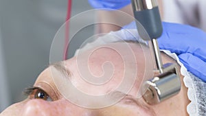 Cosmetologist makes a micro-current procedure for the face of a young woman. Forehead close-up.