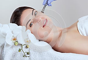The cosmetologist makes Microdermabrasion procedure of the facial skin of a beautiful, young woman in a beauty salon