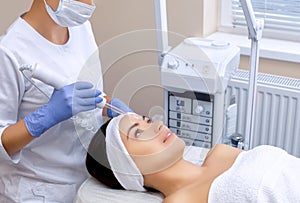 The cosmetologist makes the procedure Microcurrent therapy of the facial skin of a beautiful, young woman in a beauty salon.