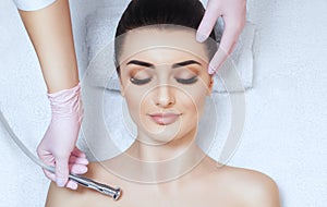 The cosmetologist makes the procedure Microdermabrasion on the collarbone and neck of a beautiful, young woman in a beauty salon