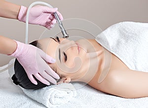 The cosmetologist makes the procedure Microdermabrasion of the facial skin of a beautiful, young woman in a beauty salon.