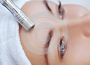 The cosmetologist makes the procedure Microdermabrasion of the facial skin of a beautiful, young woman in a beauty salon. photo