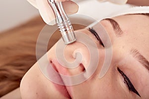 The cosmetologist makes the procedure Microdermabrasion of the facial skin of a beautiful, young woman in a beauty salon