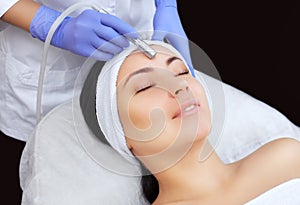 The cosmetologist makes the procedure Microdermabrasion of the facial skin of a beautiful, young woman in a beauty salon.