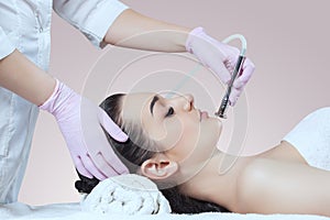 The cosmetologist makes the procedure Microdermabrasion of the facial skin of a beautiful, young woman in a beauty salon.