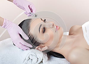 The cosmetologist makes the procedure Microdermabrasion of the facial skin of a beautiful, young woman in a beauty salon